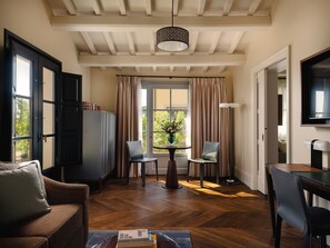 A room with a wooden floor, a sofa, a table with chairs, a cabinet, a window with curtains, and a ceiling with exposed beams.