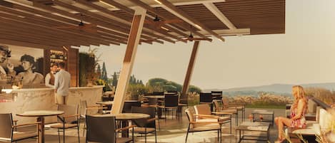 Un espacio al aire libre con mesas y sillas, una barra con un bartender, y vistas del paisaje.