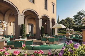 An outdoor patio with green seating, tables, and a large umbrella.
