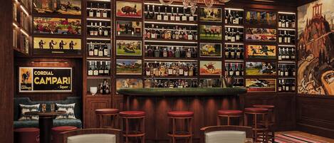 A bar area with multiple seating options, a variety of liquor bottles, and artwork on the walls.