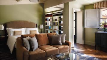 A well-lit room with a large bed, a brown sofa, a glass coffee table, and a bookshelf filled with books.
