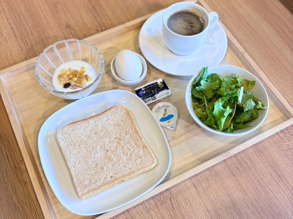 A tray with a slice of white bread, a small bowl of salad, a cup of coffee, and a container of margarine.