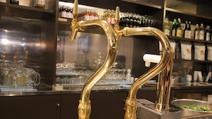 Una zona de bar con un grifo dorado y estantes llenos de bebidas embotelladas.
