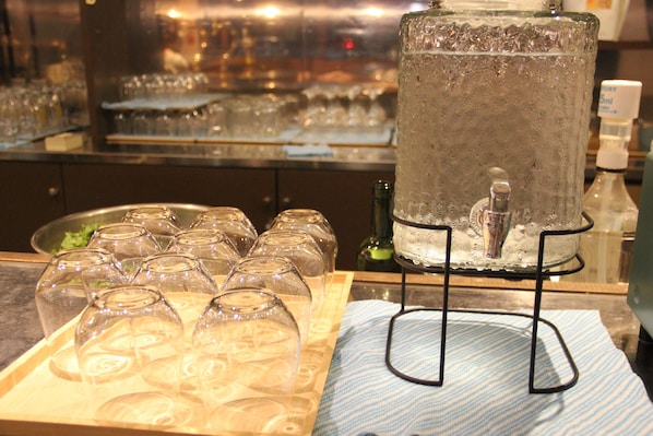 A bar area with a large ice-filled glass container, a tray of empty wine glasses, and a bottle of water. - BUNA CABIN MATSUMOTO (Matsumoto)