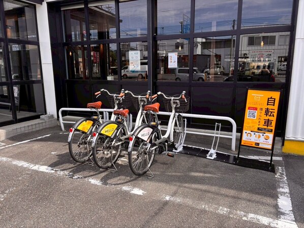 Une station de location de vélos avec trois vélos, un panneau indicateur et un bâtiment aux grandes fenêtres en arrière-plan.