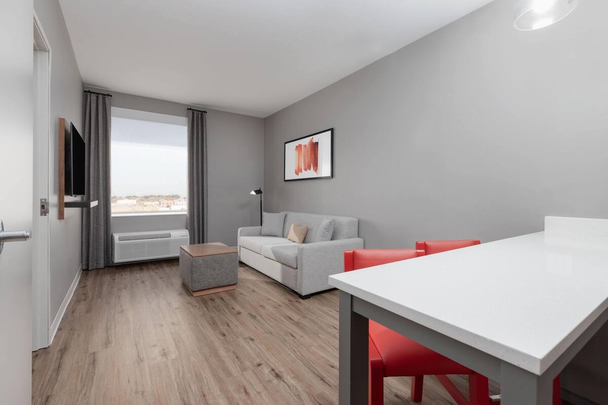 A modern room with a grey sofa, a white table, and red chairs.