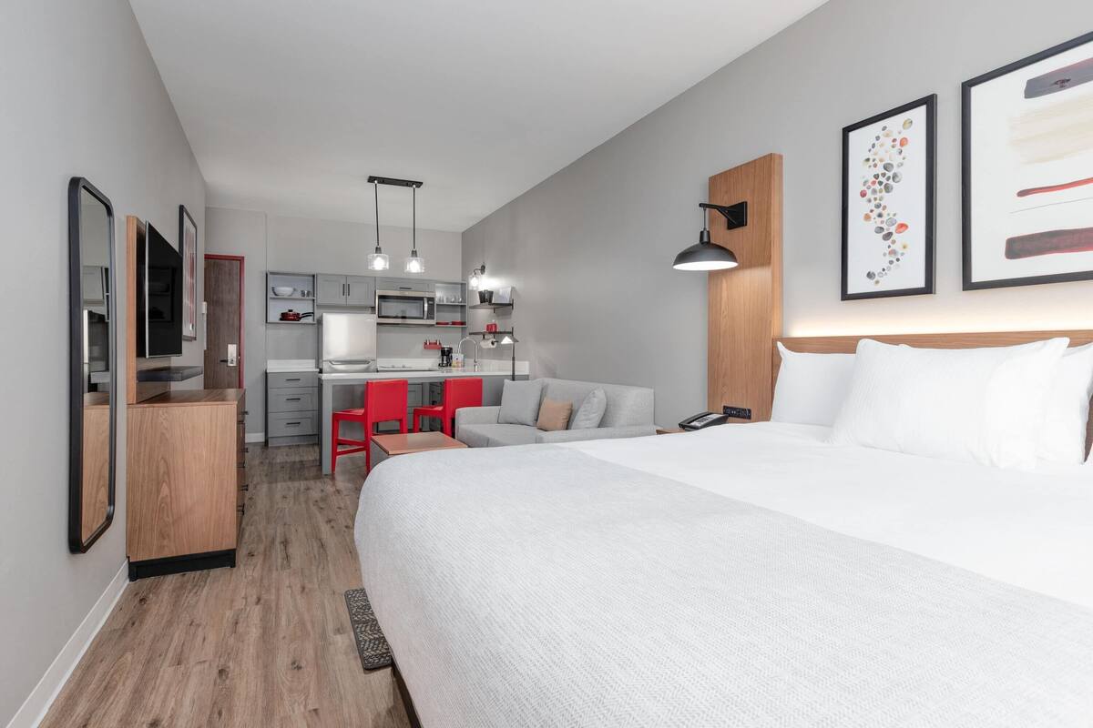 A modern hotel room with a large bed, a desk, and a kitchenette.