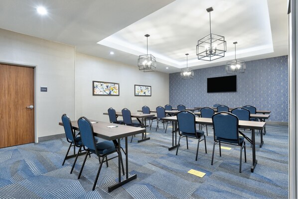 A conference room with a large screen, multiple tables, chairs, and geometric ceiling lights.