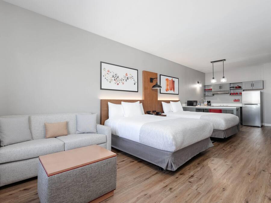 Et moderne hotelværelse med sofa, to senge, et lille tekøkken og billedkunst på væggene.