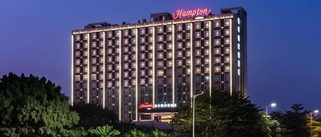 A multi-story hotel building with illuminated signage, surrounded by trees and a well-lit street.