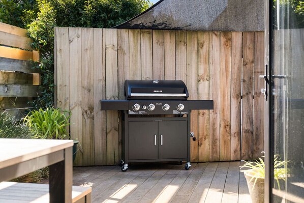 A portable grill with four controls, a storage cabinet, and a wooden fence in the background. - Coastal Tiny House Mount Maunganui (Mount Maunganui)