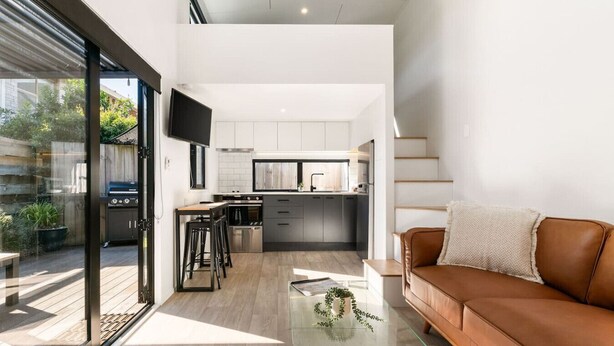 A modern kitchen with a central island, a dining area with stools, a glass coffee table, and a brown leather sofa.