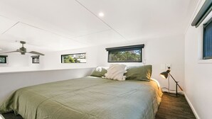 A bedroom with a large bed, a ceiling fan, a window with a view, and a desk lamp.