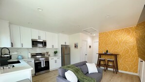A modern kitchen with white cabinets, stainless steel appliances, and a grey sofa with a green throw.