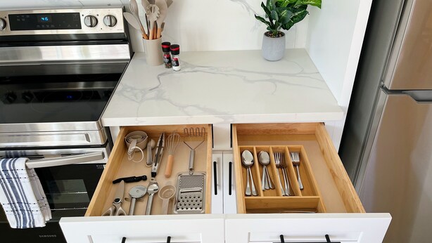 A kitchen with a marble countertop, a stainless steel oven, a drawer organizer with utensils, and a potted plant.