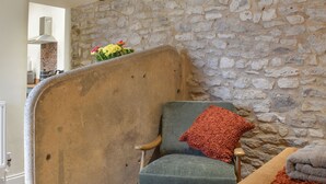 Un mur de pierre, une chaise avec un coussin et une table recouverte d’une couverture.