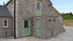 Un bâtiment en pierre avec un toit à deux versants, deux portes vertes et une allée gravillonnée.