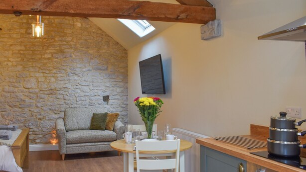 A cozy room with a stone wall, a wooden ceiling, a sofa, a dining table with chairs, a kitchen area with a stove, and a window. - 1 bedroom accommodation in Earl Sterndale, near Buxton (Earl Sterndale, near Buxton)