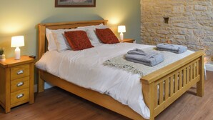 A wooden bed with white bedding, two red pillows, a lamp on each side, and a stone wall. - 1 bedroom accommodation in Earl Sterndale, near Buxton (Earl Sterndale, near Buxton)