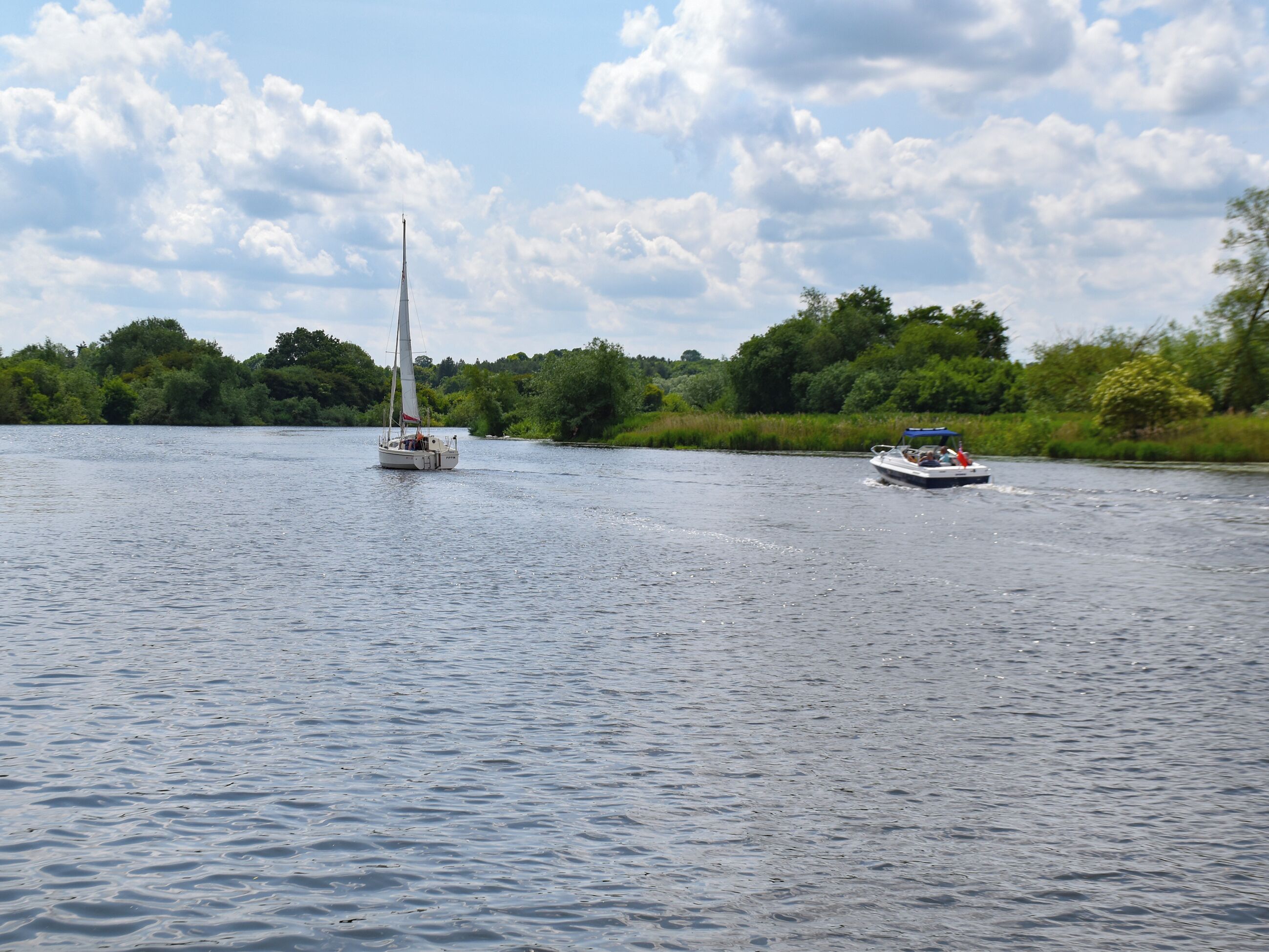 Een rustige rivier met een zeilboot en een motorboot.