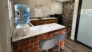 Uma cozinha com dispensador de água, bancada de mármore, parede de pedra e um banco embutido.