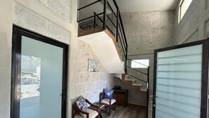 Um interior moderno com escada, área de estar e vista através de uma porta de vidro.