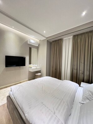Une chambre d’hôtel moderne dotée d’un grand lit, d’un téléviseur à écran plat fixé au mur, d’une coiffeuse avec un miroir et d’une fenêtre avec des rideaux.