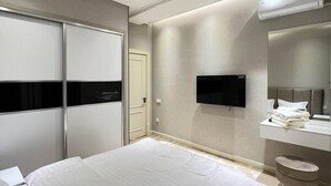 Een moderne slaapkamer met een groot bed, een flatscreen televisie aan de muur, een kaptafel met spiegel en een schuifdeurkast.