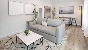 A modern living room with a gray sofa, a coffee table, and a dining area with a table and chairs. - Iris Suite I Walk to Shops, Dining + Bay (Coronado)