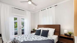 A bedroom with a bed, nightstands, a ceiling fan, and a sliding glass door leading to an outdoor area. - Iris Suite I Walk to Shops, Dining + Bay (Coronado)