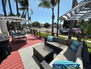 A covered outdoor seating area with a red deck, a sofa, and a table. - Iris Suite I Walk to Shops, Dining + Bay (Coronado)
