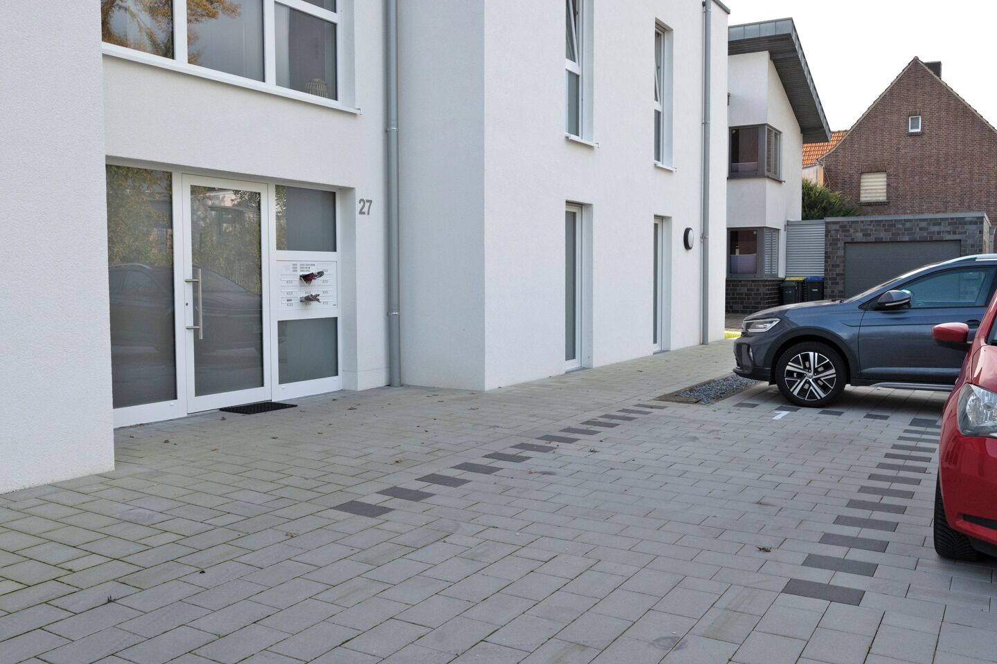 Um edifício de apartamentos moderno com um caminho pavimentado e um carro estacionado.