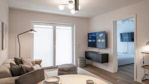 Moderni olohuone, jossa on sohva, sohvapöytä, televisio ja suuri ikkuna.