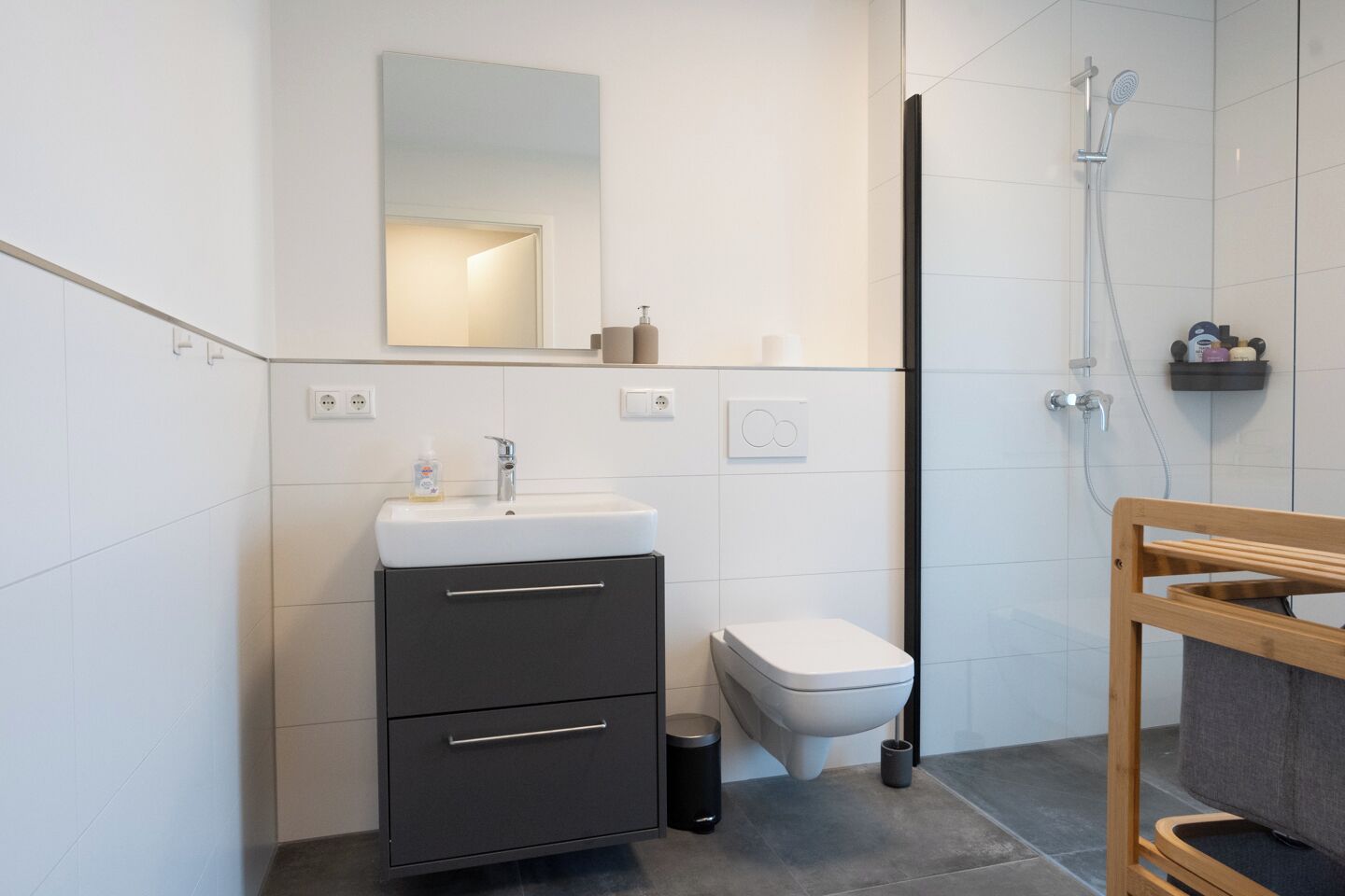 Une salle de bain moderne avec un lavabo blanc, un meuble sombre, des toilettes et un espace douche.