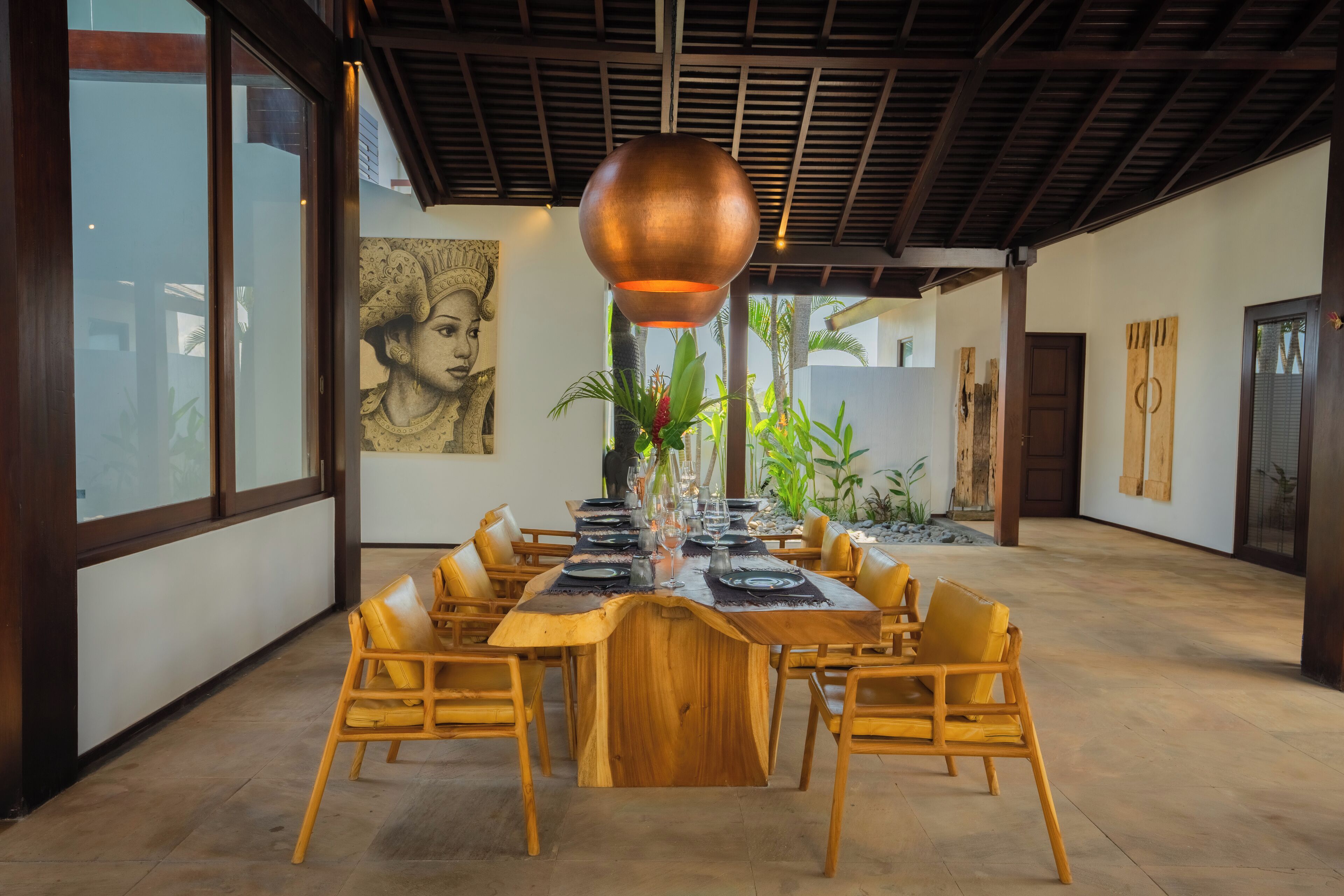 A dining area with a long wooden table set for six, surrounded by yellow chairs, under a wooden ceiling with a copper pendant light.