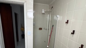 Un baño con paredes de azulejos blancos, cabina de ducha de vidrio y puerta de madera.