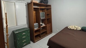 Un dormitorio con una cama, un armario de madera, un aparador verde y una ventana con persianas.