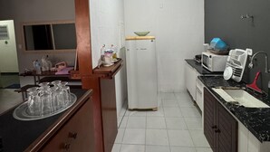 Una cocina compacta con paredes blancas, un refrigerador, un microondas, un lavamanos y un mueble de madera.