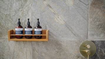 Een houten plank met drie flessen Sensatia Botanicals producten tegen een stenen muur.
