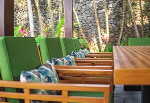 Une table en bois, des chaises à revêtement vert et des coussins à motifs.