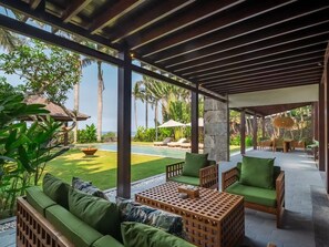 A covered outdoor seating area with a pool, lounge chairs, and a view of the pool.
