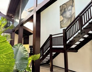 A staircase with wooden railings leading to an upper level, surrounded by large green plants.