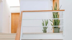 Una escalera moderna con barandillas de madera y paredes blancas, que conduce a un rellano con plantas en macetas.