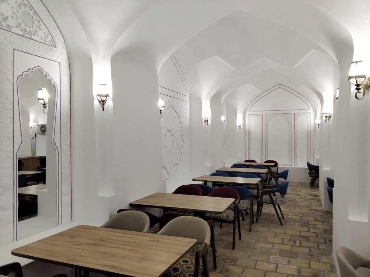 Um corredor com mesas e cadeiras, paredes brancas e iluminação decorativa.