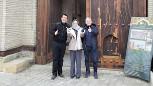 Three people standing in front of a large wooden door with a signboard to the right. - Hotel Caravansaray Rashid in Bukhara  (Bukhara)