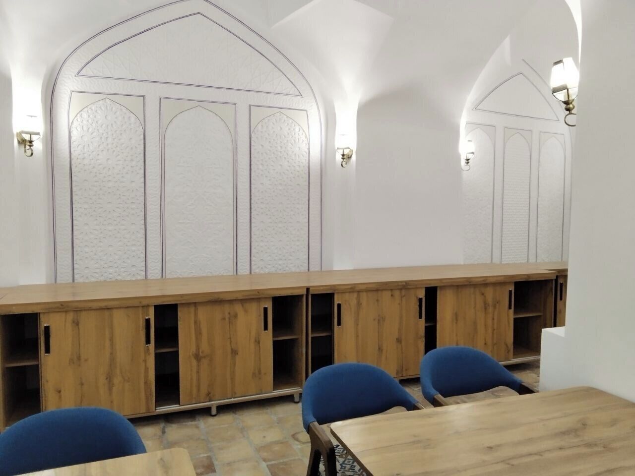 Um quarto com uma mesa comprida de madeira, cadeiras azuis e uma parede branca com desenhos decorativos.
