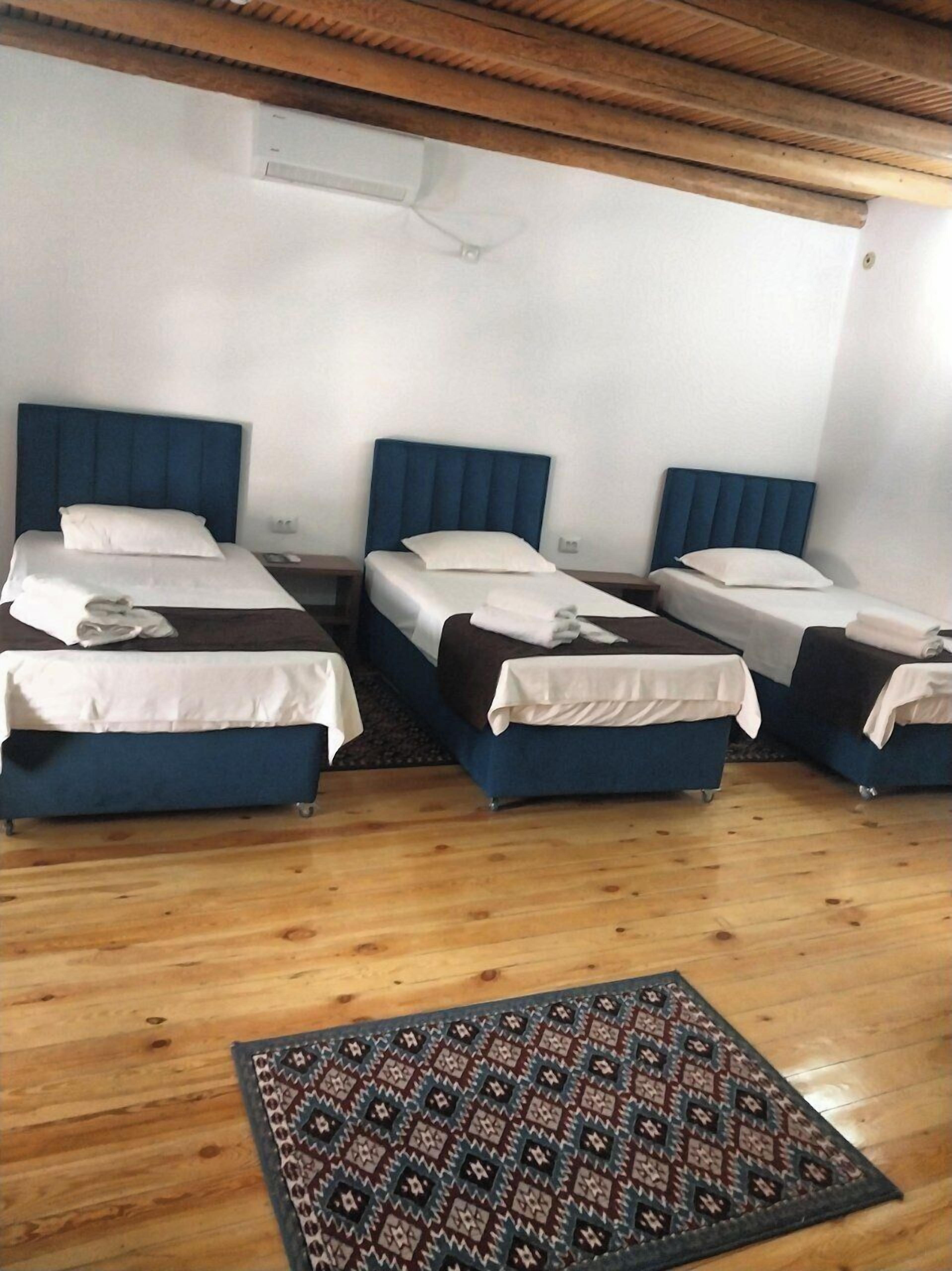 Une chambre d’hôtel avec trois lits simples, un tapis à motifs, un plancher en bois et un plafond en bois.