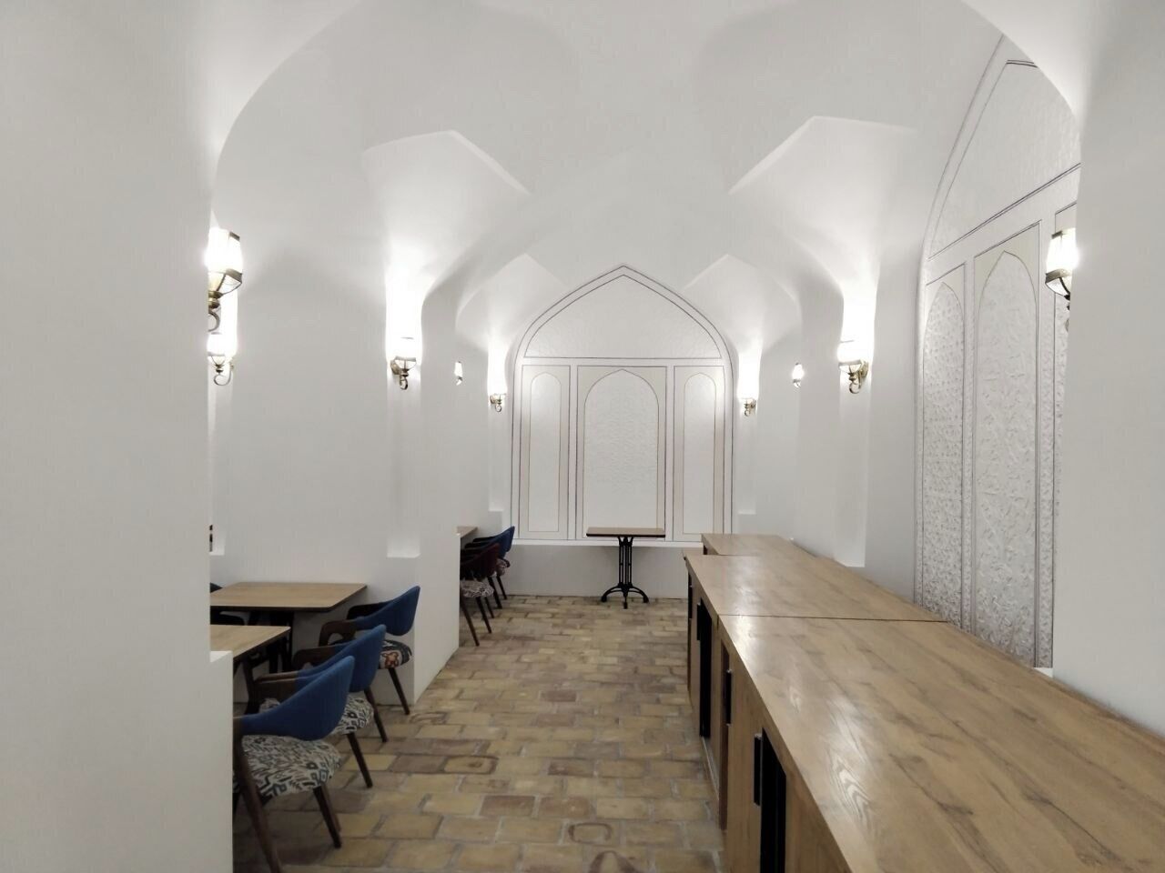 Una habitación alargada y estrecha con una mesa y sillas de madera, paredes blancas y un suelo estampado.