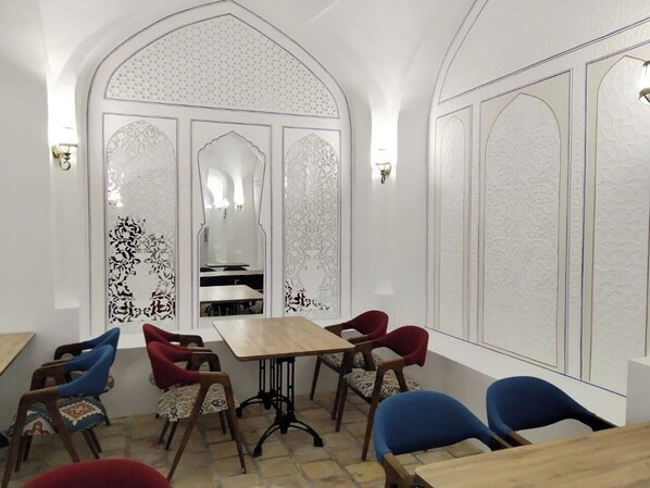 A dining area with a central table, surrounded by chairs, and a decorative wall with intricate patterns. - Hotel Caravansaray Rashid in Bukhara (Bukhara)