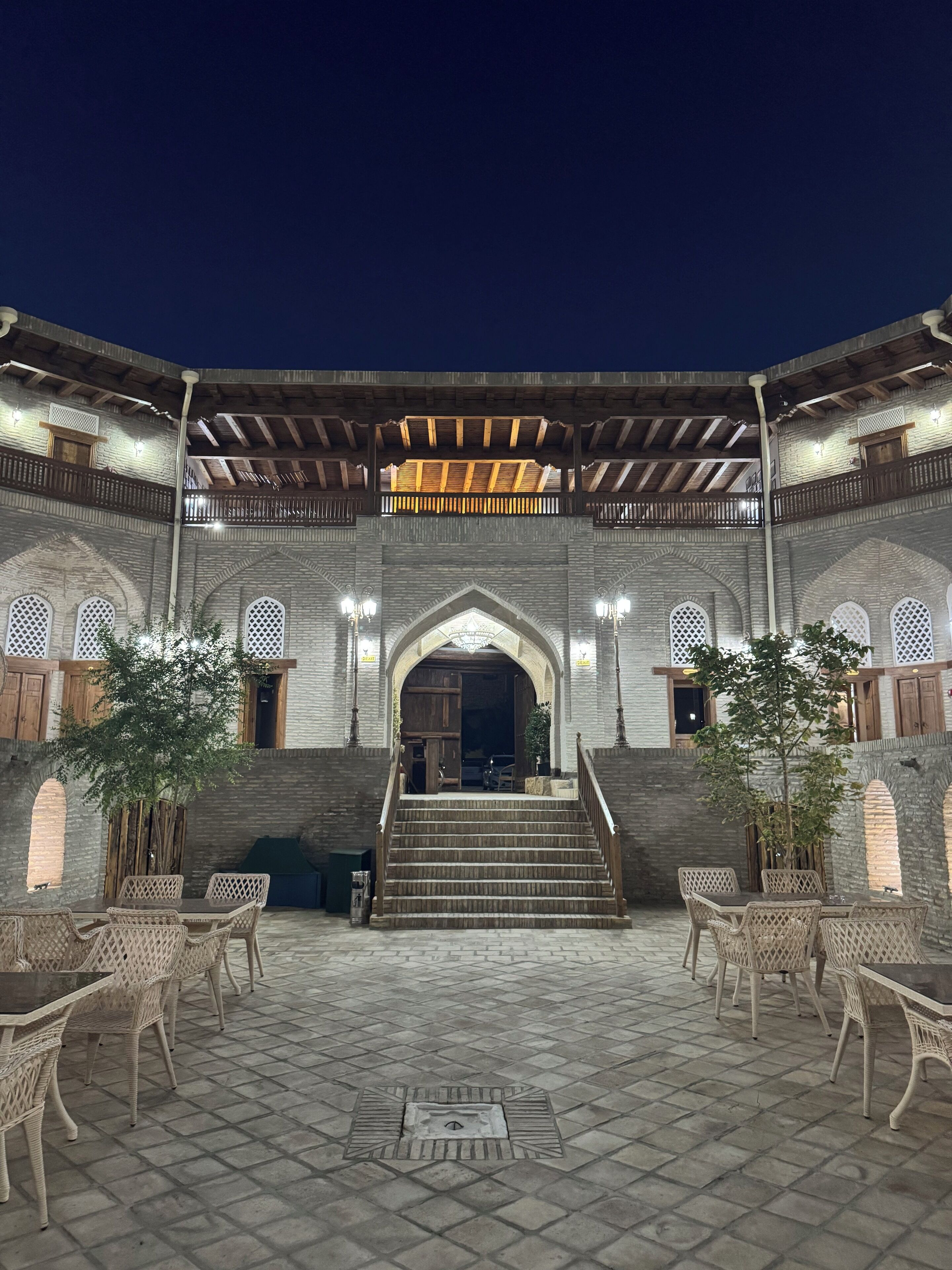 A courtyard with a stone staircase leading to an entrance, surrounded by wicker furniture and potted plants.
